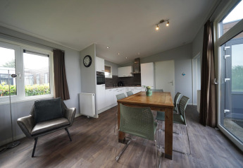 Soggiorno e cucina moderni nel lodge L-Pavilion 6 a De Biesbosch, Paesi Bassi, con tavolo e poltrona.