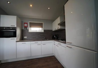 Cucina moderna nel L-Pavilion 6 a De Biesbosch, Paesi Bassi, con mobili bianchi e pavimento in legno.