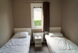 Simple bedroom with two single beds, a window, and a nightstand at L-Pavilion 6 in De Biesbosch, Netherlands.