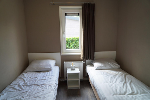 Dormitorio sencillo con dos camas individuales, una ventana y una mesita de noche en L-Pavilion 6 en De Biesbosch, Países Bajos.