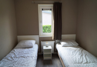 Dormitorio sencillo con dos camas individuales, una ventana y una mesita de noche en L-Pavilion 6 en De Biesbosch, Países Bajos.
