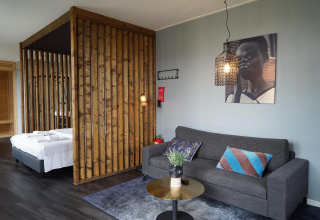 Moderne lodge met houten schutting, grijze zetel, kleurrijke kussens en muurkunst bij Marina Strandbad, Nederland.