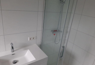 Bagno moderno con lavabo bianco, doccia e piastrelle bianche presso Mode Wellness 2 al Marina Strandbad, Paesi Bassi.
