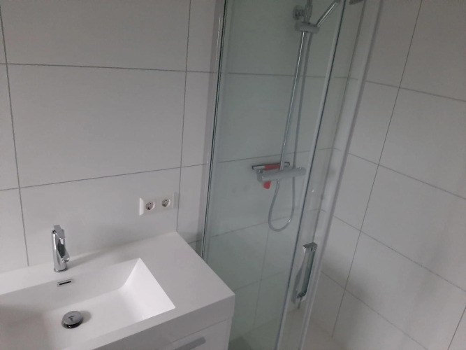 Baño moderno con lavabo blanco, ducha y azulejos blancos en Mode Wellness 2 en Marina Strandbad, Países Bajos.