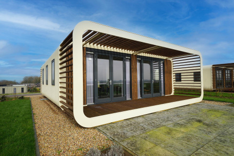 Moderne lodge met ronde gevel en houten lamellen bij Marina Strandbad in Nederland, zonnige dag.