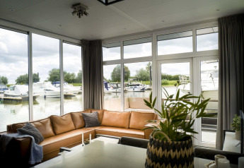 Wohnzimmer mit großen Fenstern und Blick auf Boote am Hafen in Water lodge 4, Marina Strandbad, Niederlande.