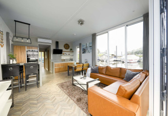 Moderne stue på husbåd Water lodge 4 ved Marina Strandbad i Holland med store vinduer og lædersofa.