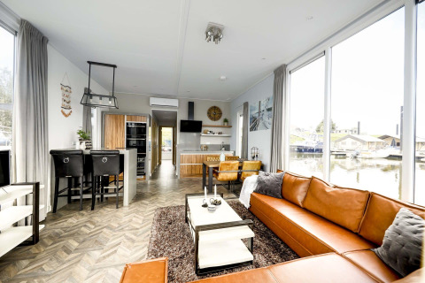 Modern interieur op woonboot Water lodge 4 in Marina Strandbad, Nederland, met grote ramen en lederen zetel.