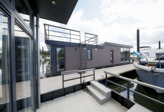 Moderne woonboot Water Lodge 4 bij Marina Strandbad in Nederland met terras, trap en aangemeerde boten.