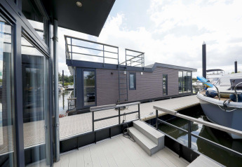 Moderne woonboot Water Lodge 4 bij Marina Strandbad in Nederland met terras, trap en aangemeerde boten.