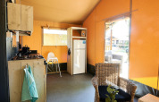 Interior de tienda safari en Wilsumer Berge, Alemania, con cocina, nevera y silla de mimbre.