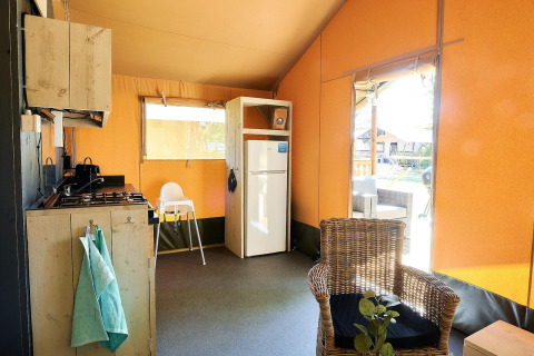 Interno di una tenda safari a Wilsumer Berge, Germania, con cucina, frigorifero e sedia in vimini.