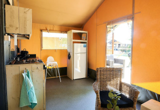 Interno di una tenda safari a Wilsumer Berge, Germania, con cucina, frigorifero e sedia in vimini.