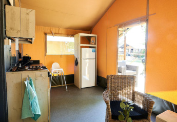 Interieur van safaritent op Wilsumer Berge in Duitsland met keuken, koelkast en rotan stoel.