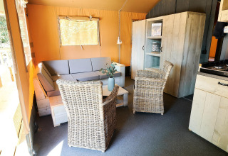 Binnenzicht van een safaritent bij Wilsumer Berge in Duitsland met zetel, stoelen en houten kasten.