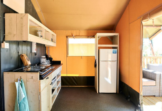 Kitchen area inside a safari tent lodge at Wilsumer Berge, Germany, with stove, fridge, and outdoor seating.