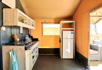 Kitchen area inside a safari tent lodge at Wilsumer Berge, Germany, with stove, fridge, and outdoor seating.