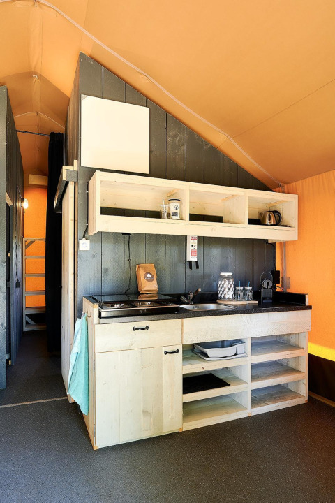 Area cucina interna di una tenda Safari al Wilsumer Berge, Germania, con scaffali in legno e fornello.