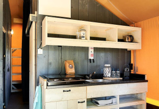 Area cucina interna di una tenda Safari al Wilsumer Berge, Germania, con scaffali in legno e fornello.