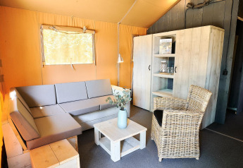 Wohnbereich im Safari-Zelt von Wilsumer Berge, Deutschland, mit grauem Sofa, Rattanstuhl und Holzschrank.