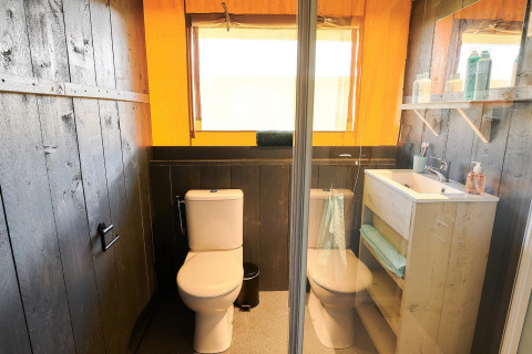Baño moderno en una cabaña con dos inodoros, lavabo, espejo, paredes y estantes de madera oscura y toallas.