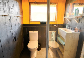 Baño moderno en una cabaña con dos inodoros, lavabo, espejo, paredes y estantes de madera oscura y toallas.