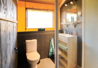 Baño en tienda safari en Wilsumer Berge, Alemania, con inodoro, lavabo, espejo y luz natural.