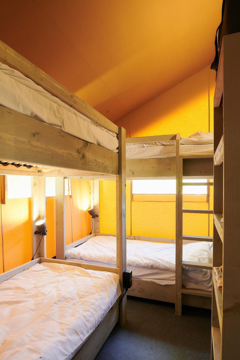 Interior view of a Safari tent at Wilsumer Berge, Germany, showing four wooden bunk beds and yellow walls.