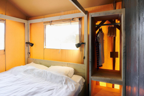 Interno di una tenda safari al Wilsumer Berge in Germania con letto, lampade e armadio aperto.