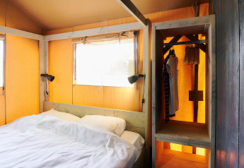 Interior de una tienda safari en Wilsumer Berge, Alemania, con cama, lámparas y armario abierto.