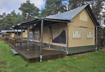Tienda safari con terraza de madera en Wilsumer Berge, Alemania, rodeada de árboles y césped verde.