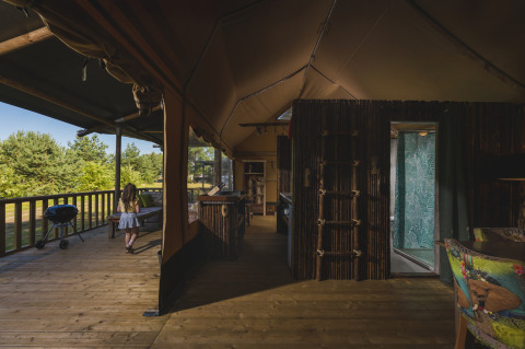 Tienda safari en Wilsumer Berge, Alemania, con terraza de madera, vista interior y una niña afuera.