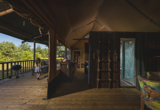Tienda safari en Wilsumer Berge, Alemania, con terraza de madera, vista interior y una niña afuera.