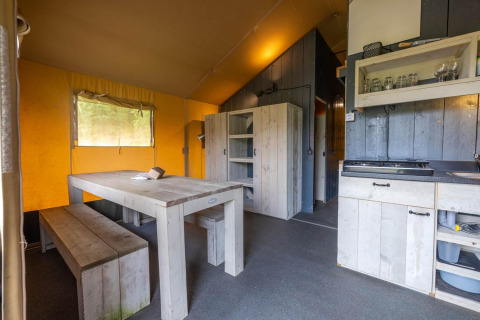 Interno di una tenda safari a Wilsumer Berge, Germania, con tavolo da pranzo, panche e angolo cucina.