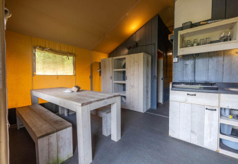 Interior de una tienda safari en Wilsumer Berge, Alemania, con mesa de comedor, bancos y cocina.