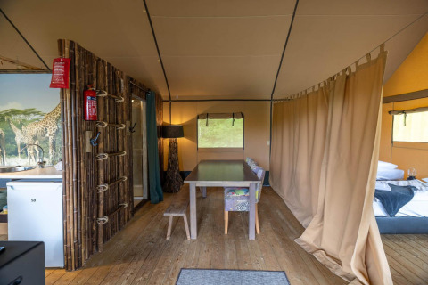 Interior de una tienda safari en Wilsumer Berge, Alemania, con mesa de comedor, cama y cortina divisoria.