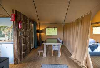 Interior de una tienda safari en Wilsumer Berge, Alemania, con mesa de comedor, cama y cortina divisoria.