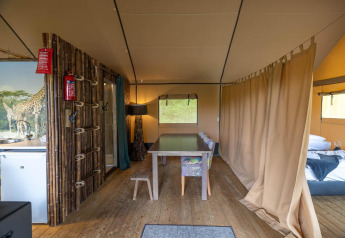 Interior de una tienda safari en Wilsumer Berge, Alemania, con mesa de comedor, cama y cortina divisoria.