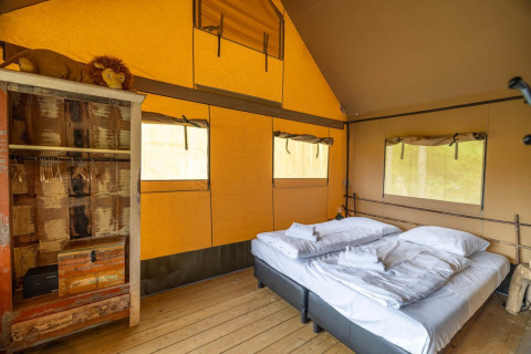 Interior de tienda safari en Wilsumer Berge, Alemania, con cama doble y armario rústico visible.