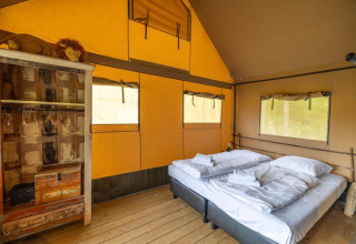 Interior de tienda safari en Wilsumer Berge, Alemania, con cama doble y armario rústico visible.