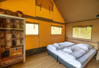 Interior de tienda safari en Wilsumer Berge, Alemania, con cama doble y armario rústico visible.