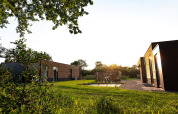Buitenaanzicht van vakantieverblijf Amalia 4 met hottub tussen moderne lodges en natuur bij zonsondergang.