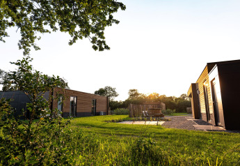 Vue extérieure de la villa de vacances Amalia 4 avec jacuzzi, lodges modernes et verdure au coucher du soleil.