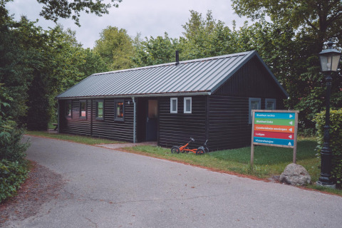 Eine schwarze Holzhütte auf einem Glamping-Platz mit buntem Wegweiser und Kinderdreirad im Gras.