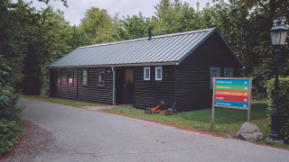 A black wooden cabin at a glamping site with a colorful signpost and a small tricycle on the grass.