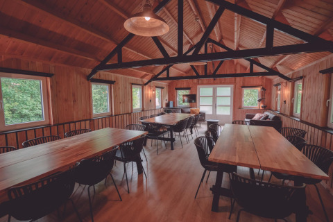 Espaciosa sala común con paredes de madera, grandes mesas y sillas en un alojamiento de glamping.