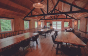 Espaciosa sala común con paredes de madera, grandes mesas y sillas en un alojamiento de glamping.
