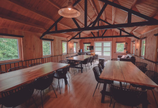 Espaciosa sala común con paredes de madera, grandes mesas y sillas en un alojamiento de glamping.