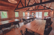 Sala comune rustica con pannelli in legno, grandi tavoli, sedie nere e divani in un glamping.