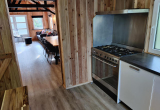 Cocina y sala de estar con paredes de madera y estufa moderna en el glamping Groupaccommodation 'de Blokhut'.